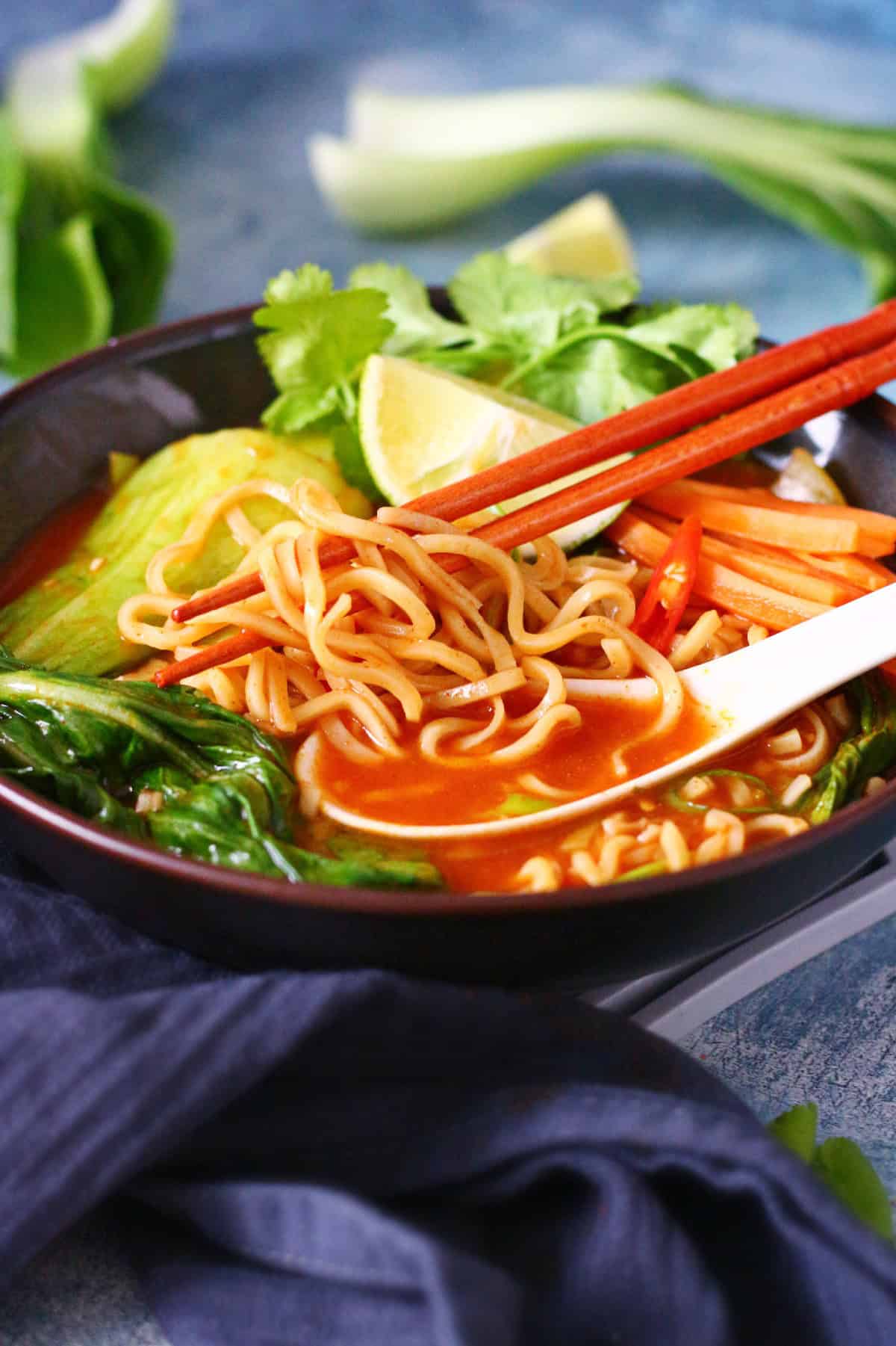 Bowl of noodle soup with spoon and chopsticks intertwined in the noodles.