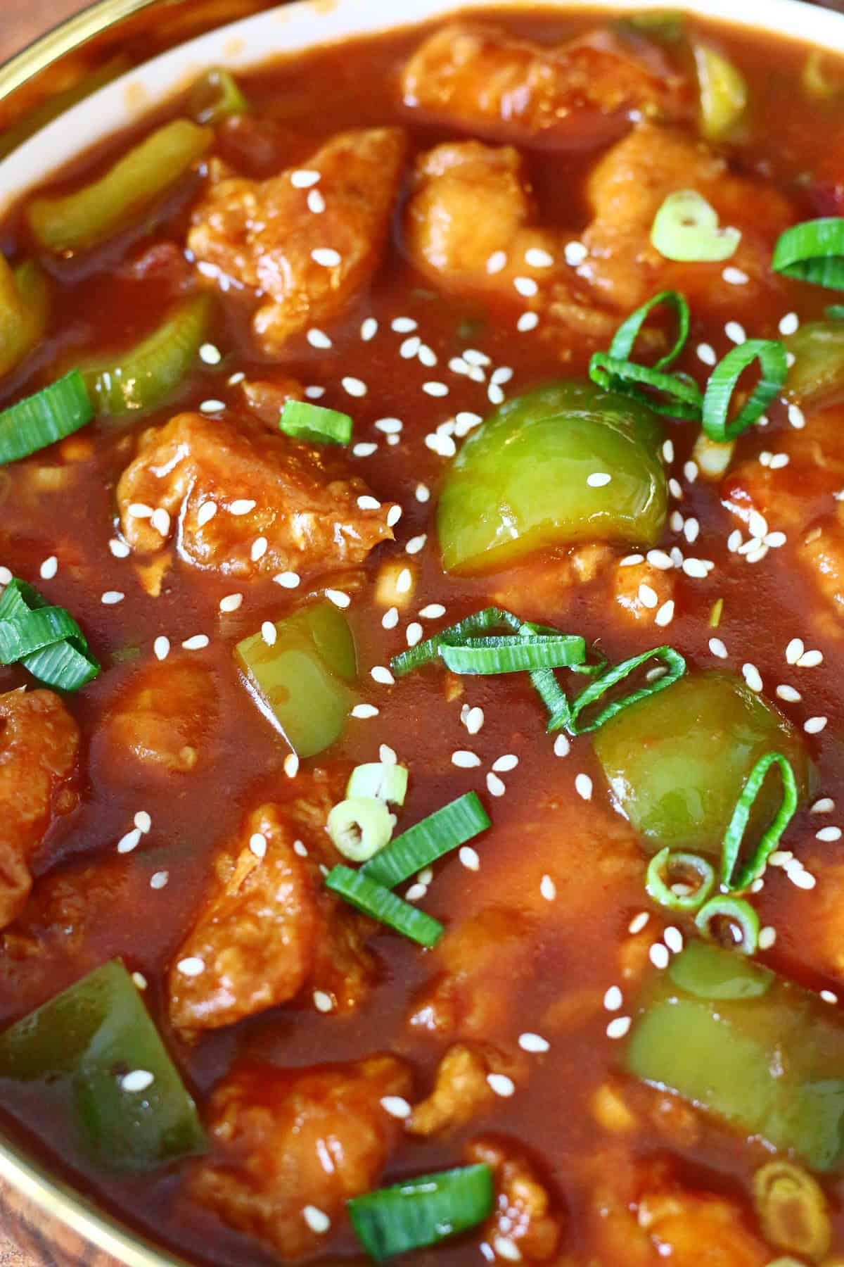 Close up of chicken Manchurian with gravy and bell peppers. garnished with green onions and sesame seeds.