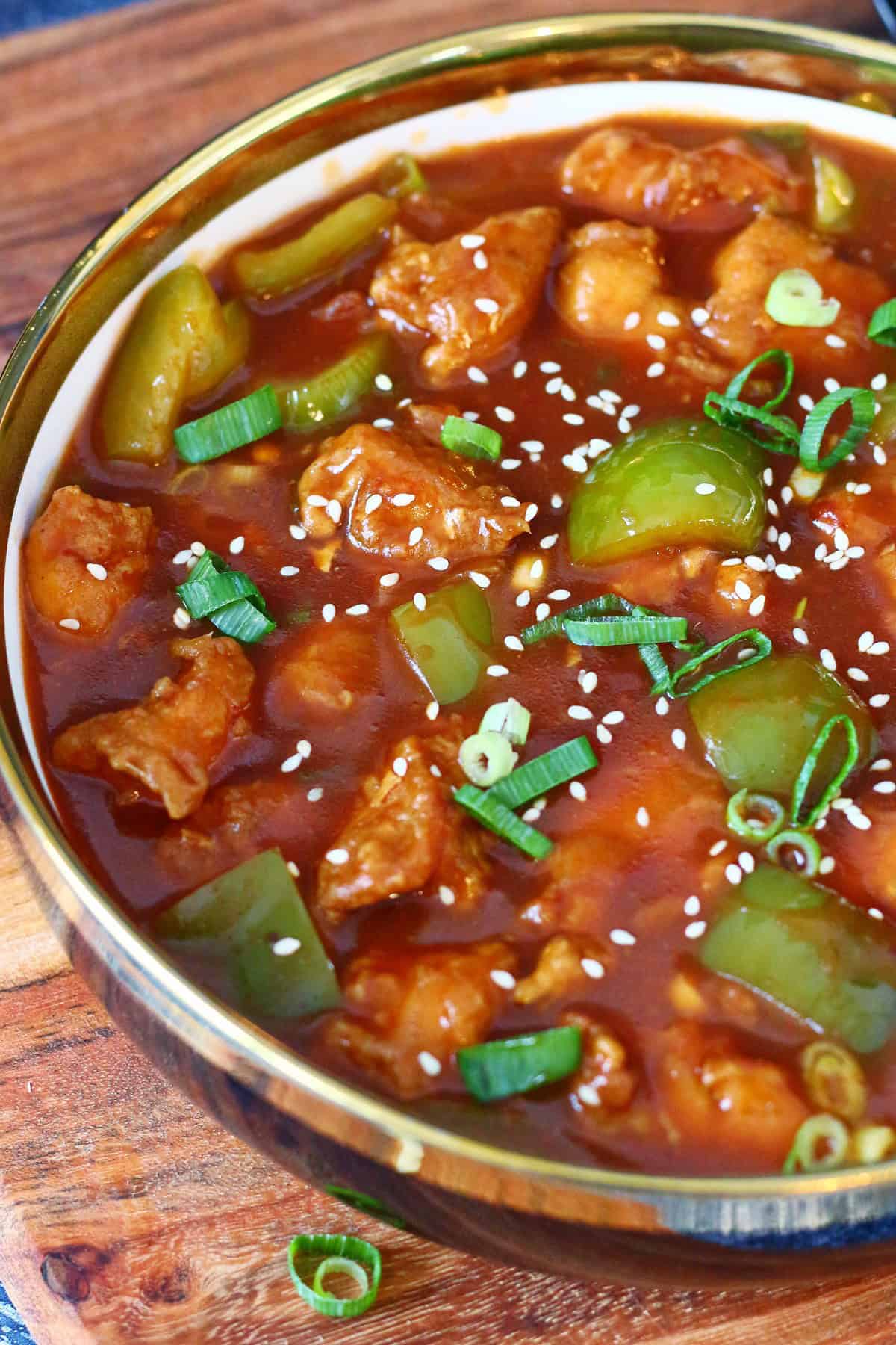 Chicken Manchurian in a bowl with bell pepper, green onions, sesame seeds and lots of sauce.