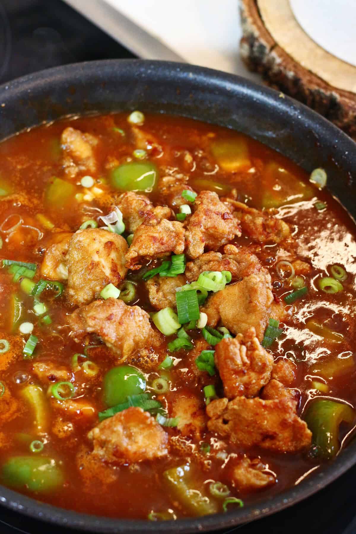 Crispy chicken with green onions on top of a red Manchurian sauce.