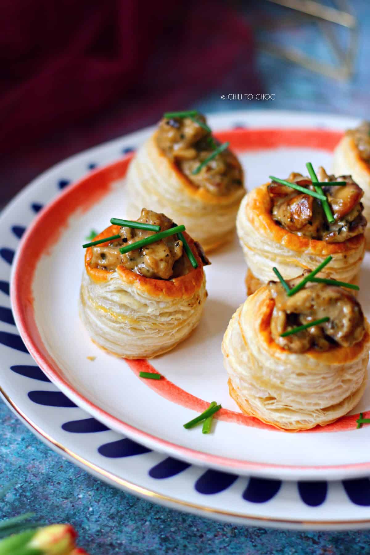 A group of vol au vents on an orange and white plate garnished with chives.