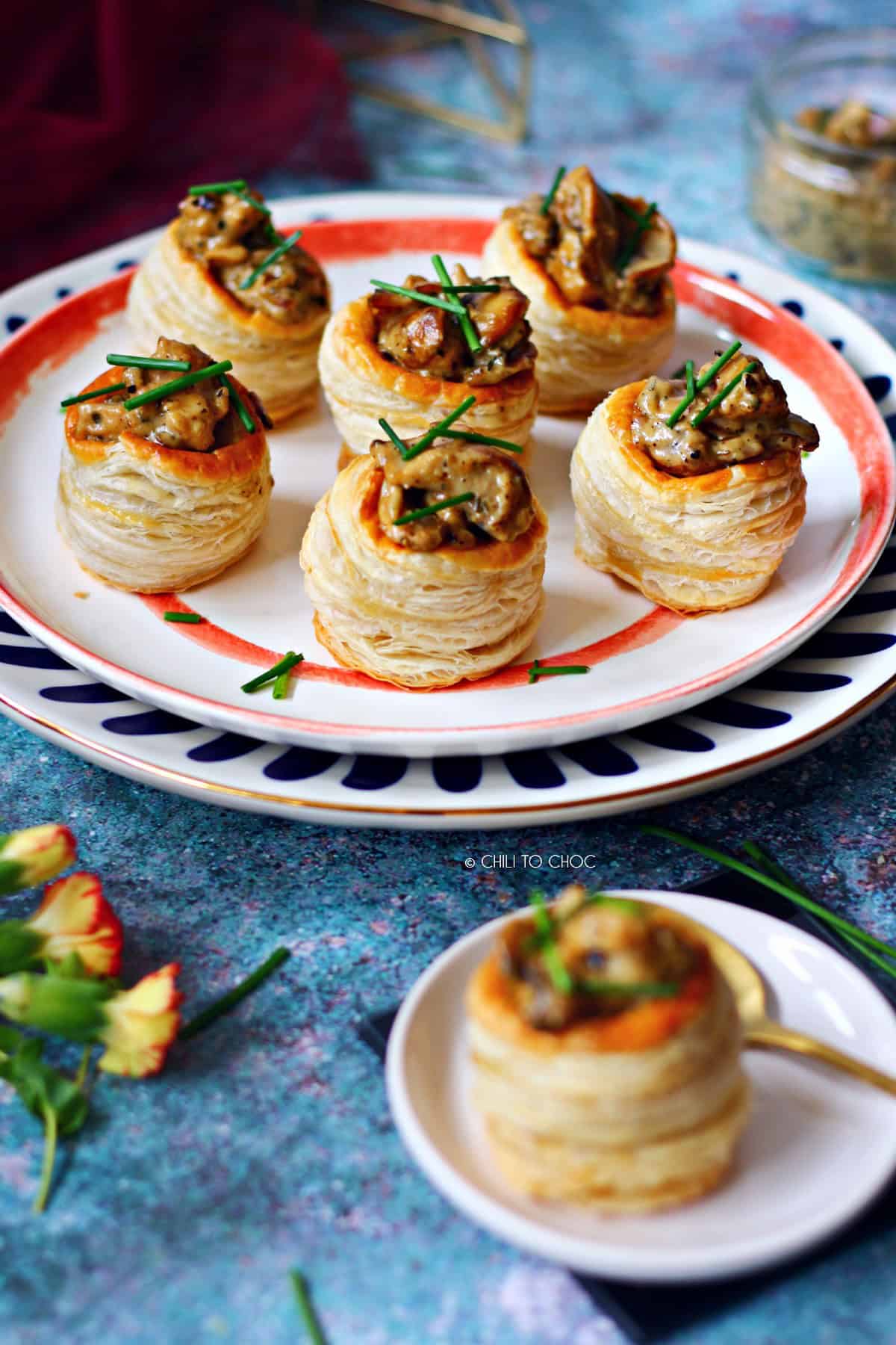 A group of six vol au vents on a set of plates with one vol au vent at the front.