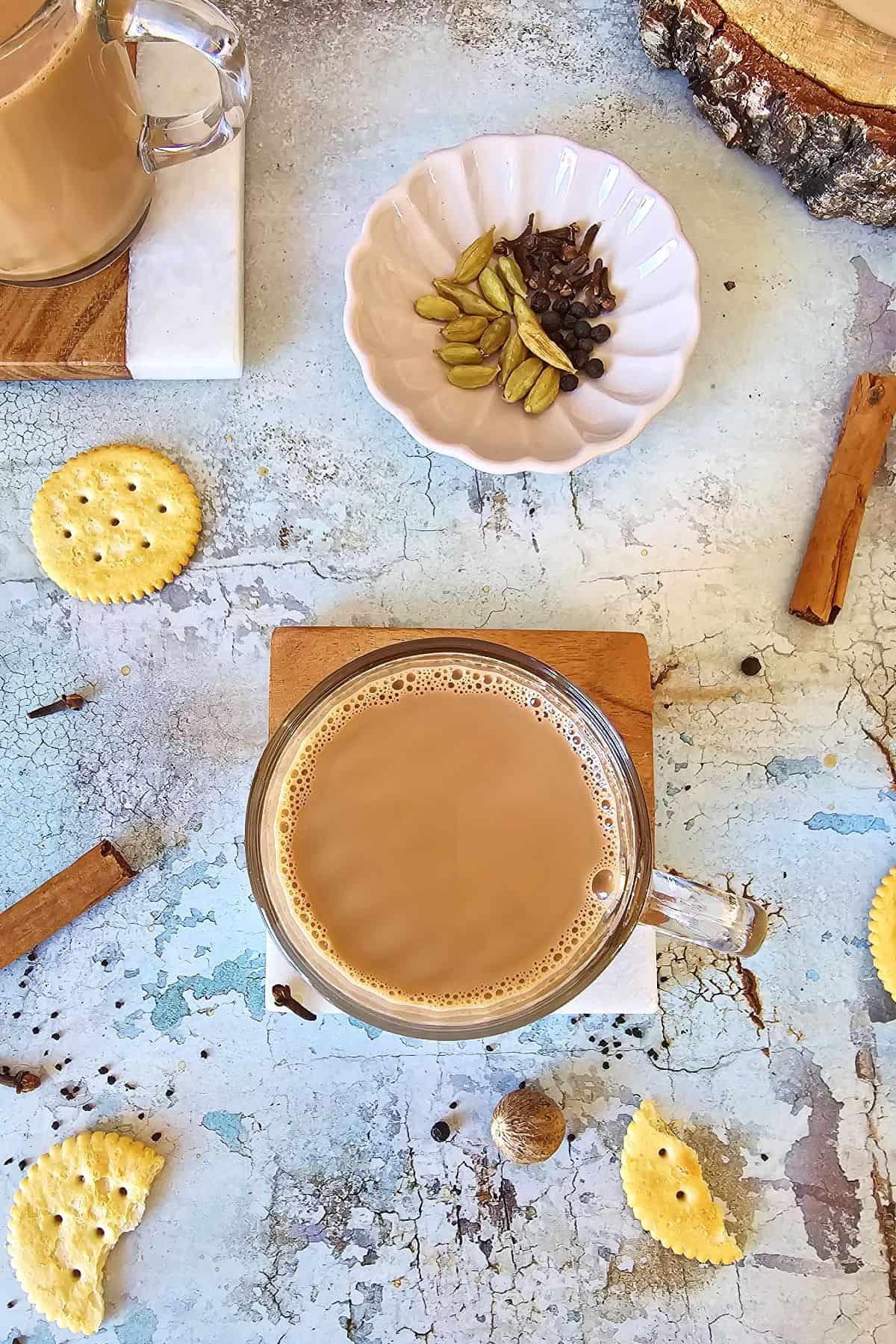 Top shot of masala chai in a mug surrounded by its ingredients.