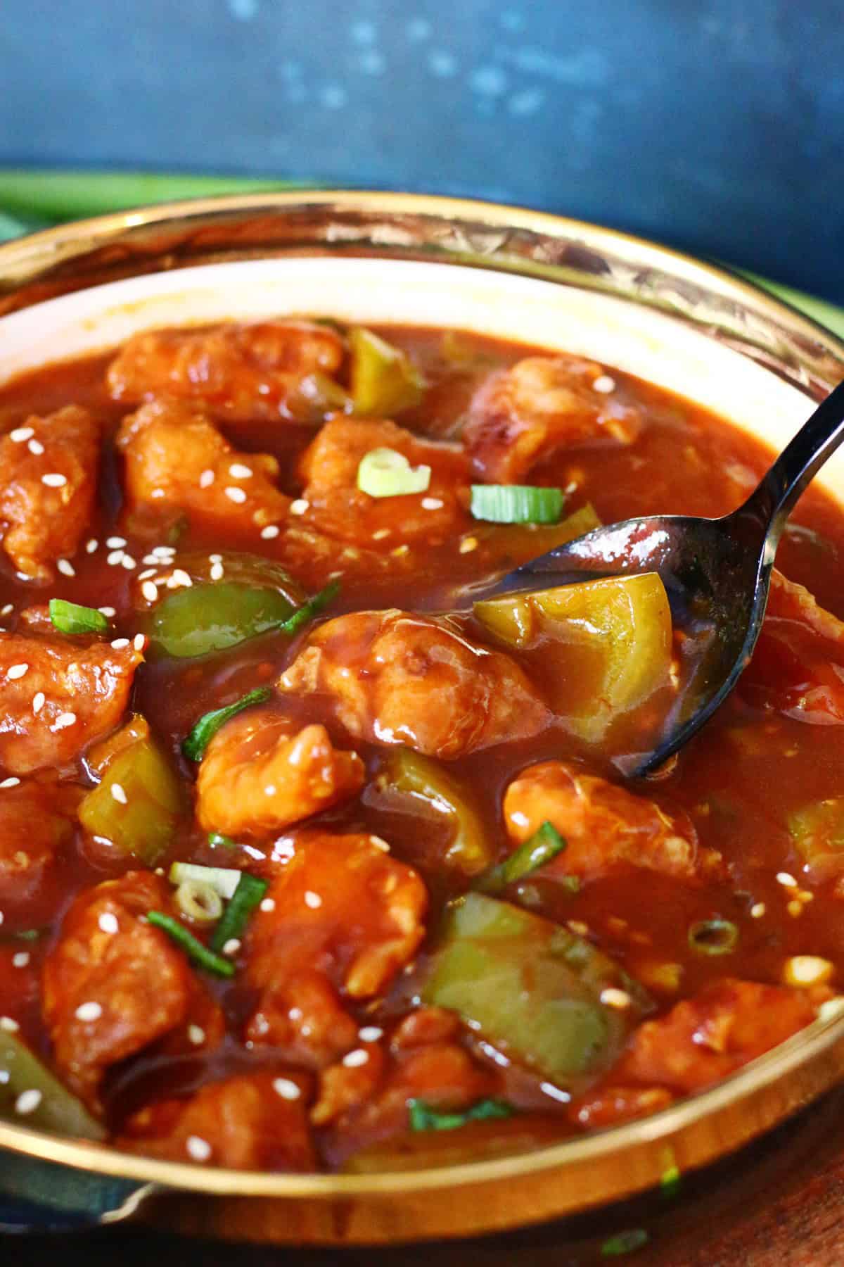 A serving spoon in a bowl containing Chicken Manchurian with sauce.