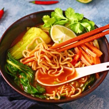 Asian noodle soup in a bowl with soup spoon and chopsticks.