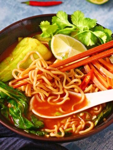 Asian noodle soup in a bowl with soup spoon and chopsticks.