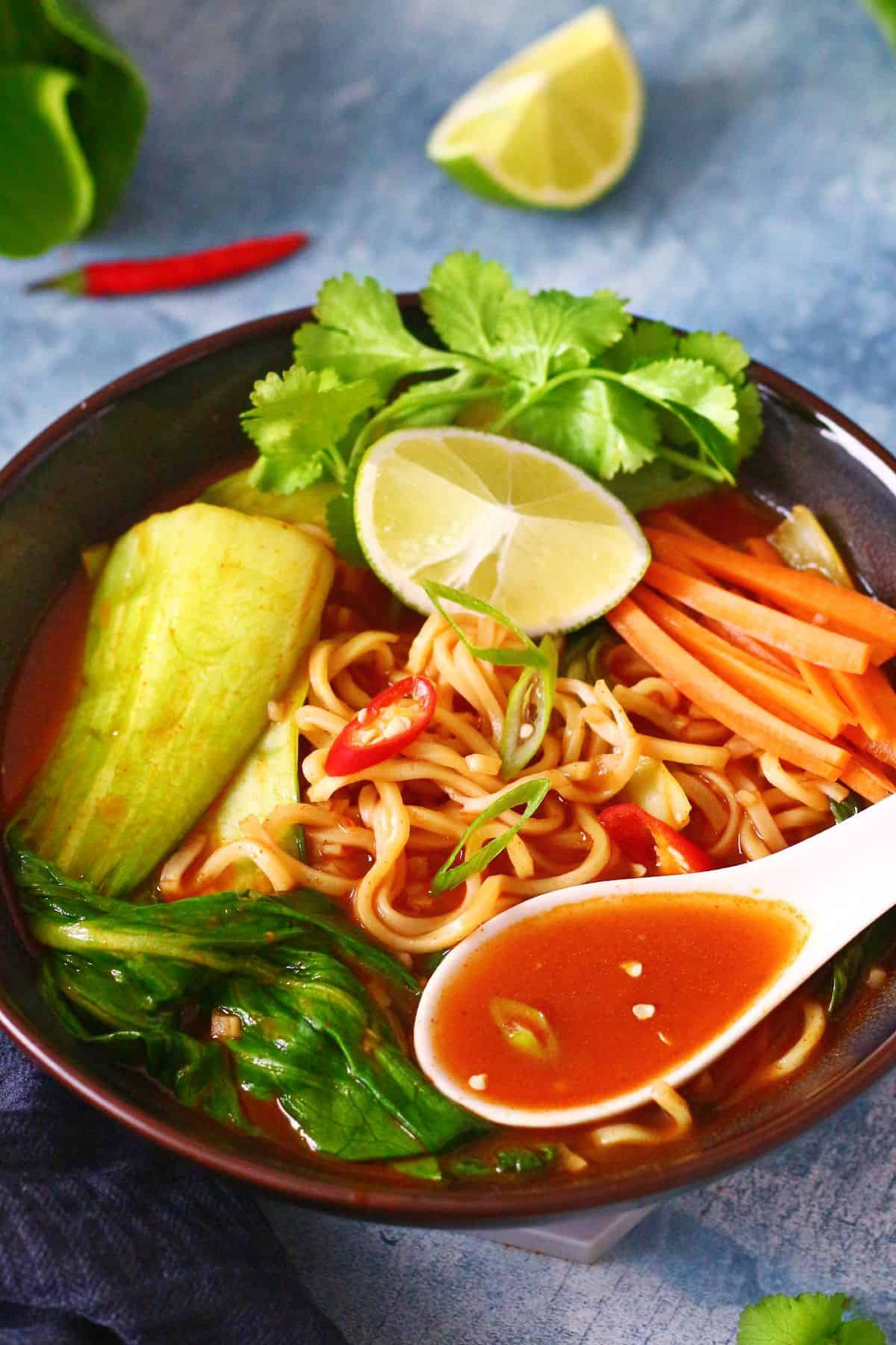 A bowl of noodle soup with toppings and some orange broth in the soup spoon.