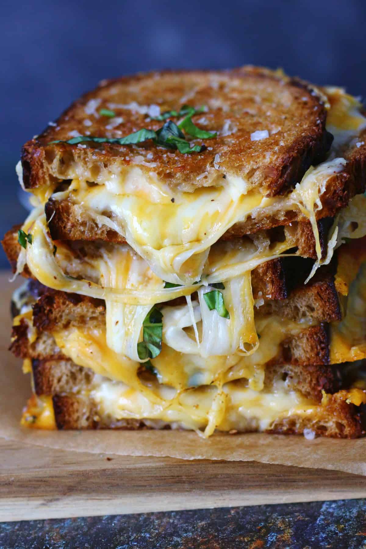 Four halves of grilled cheese sandwiches stacked with oozing cheese.