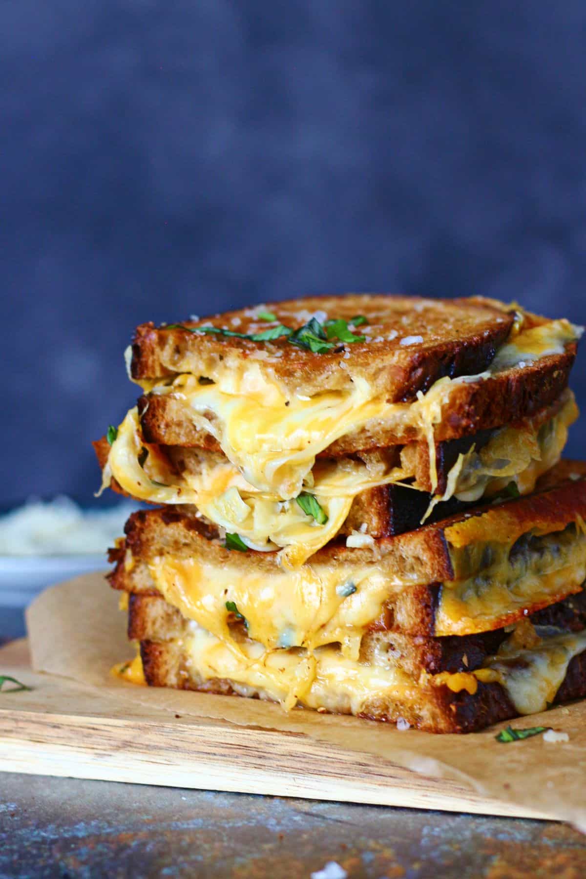 Stacked sourdough grilled cheese sandwiches cut in halves on a parchment paper and wooden board.