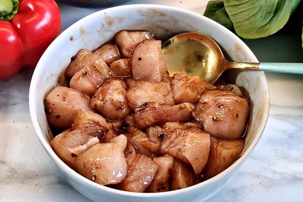 Marinated raw chicken in a grey bowl with spoon.