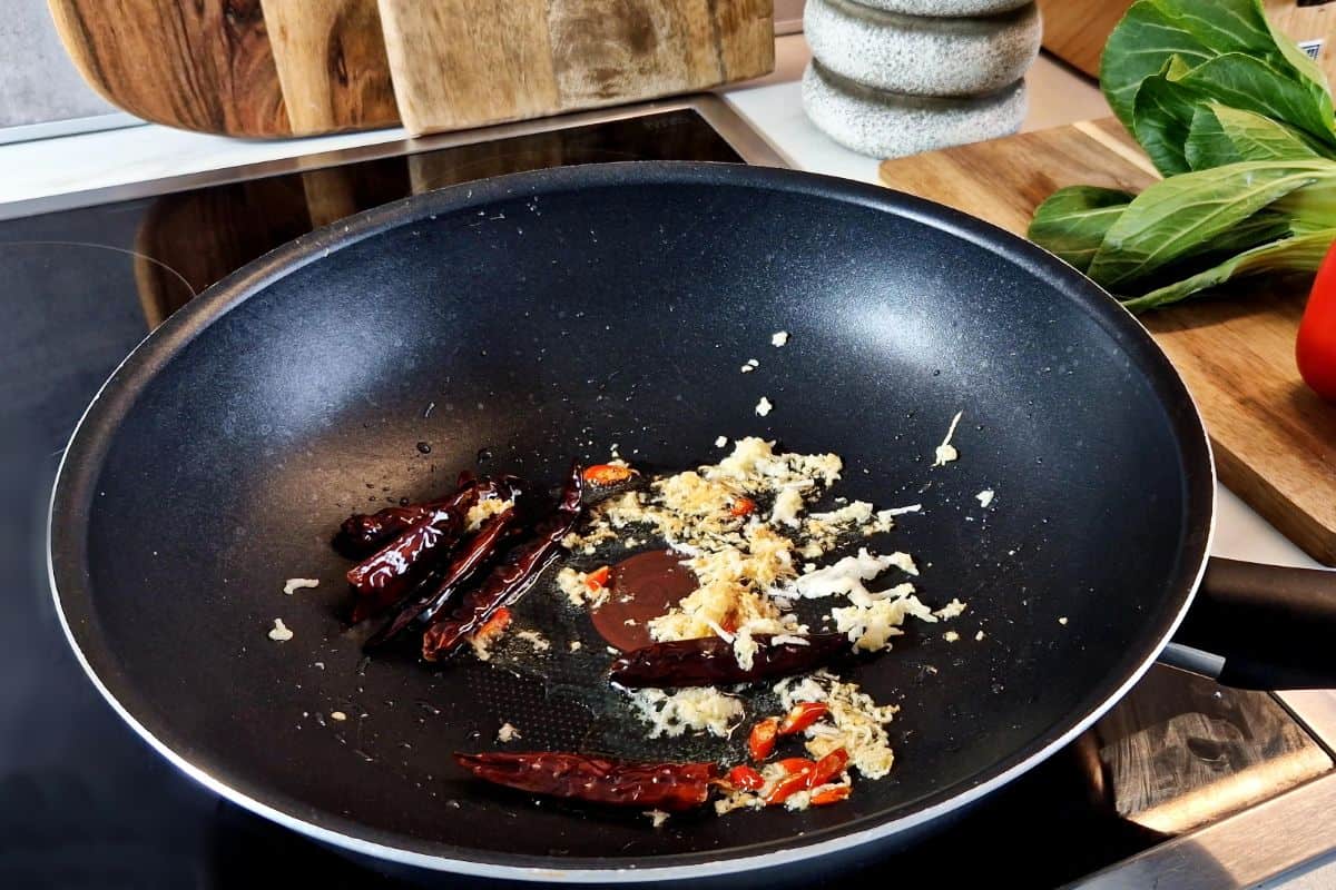 Aromatics and chilies being cooked in a wok.