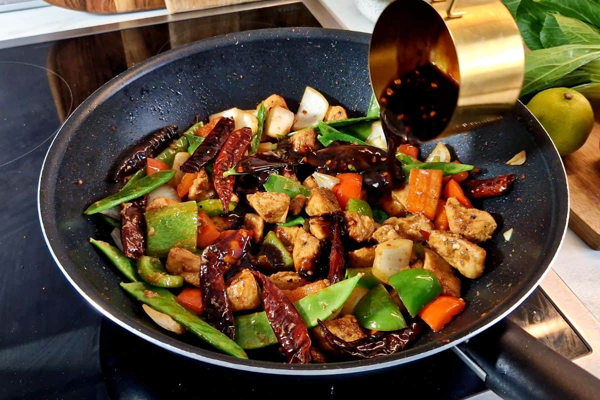 Pouring sauce in a wok with chicken and vegetables.