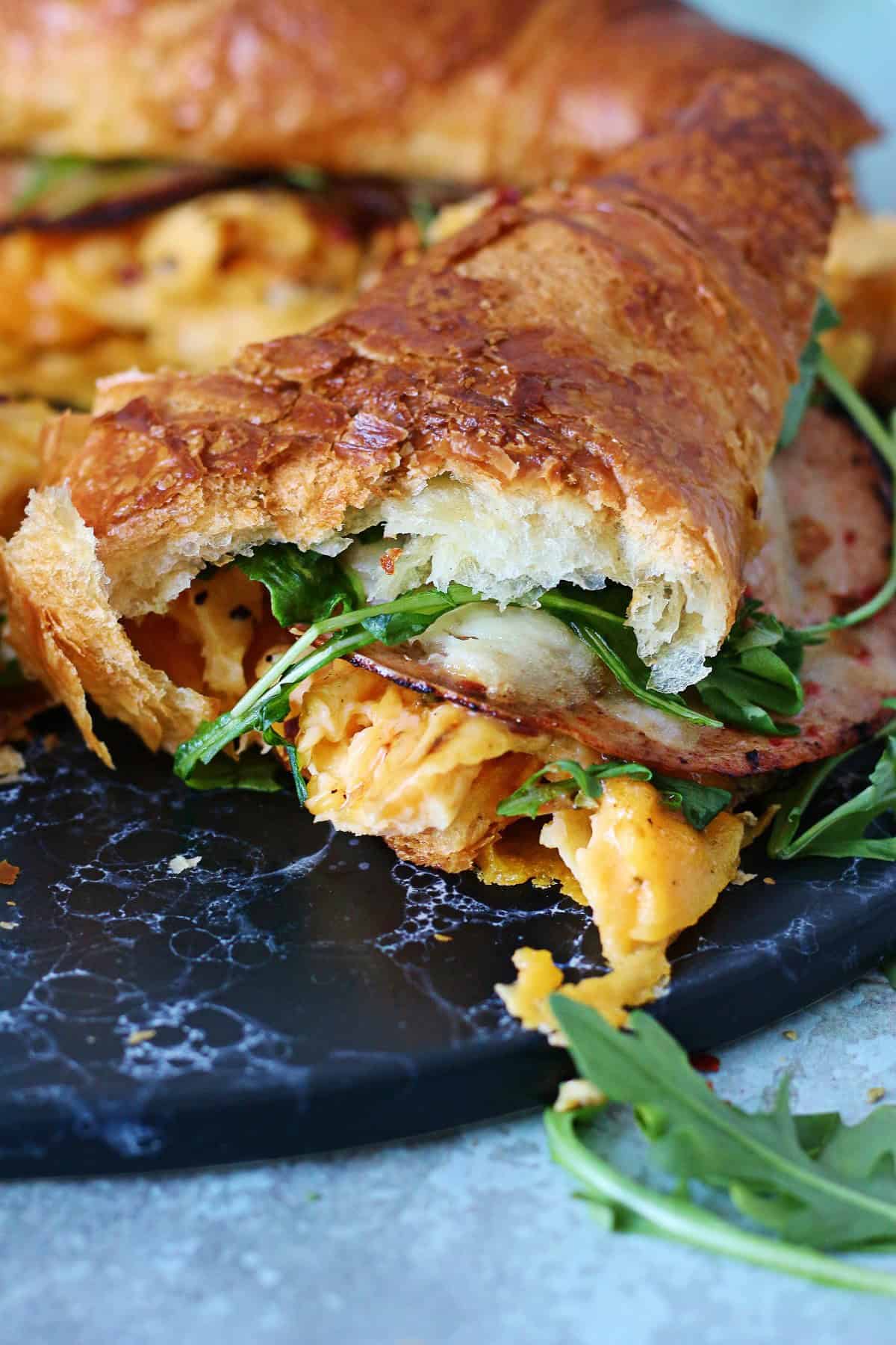 Torn apart half of a croissant sandwich with eggs, mortadella, cheese and arugula.