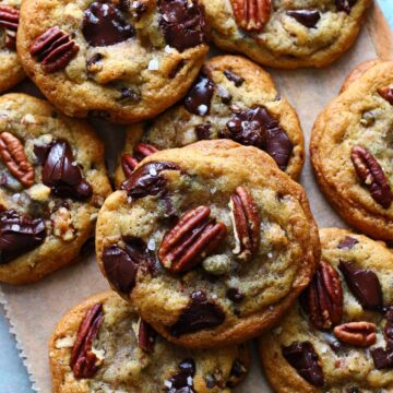 Pecan chocolate chip cookies with melted chocolate, pecan halves, and flaky sea salt on parchment paper.