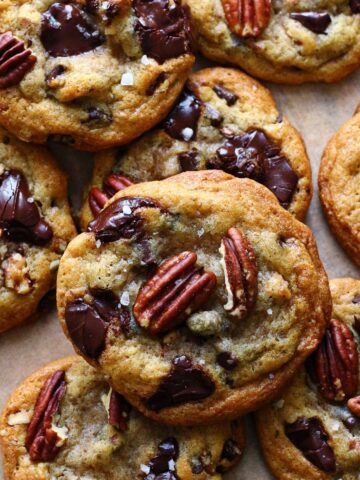 Pecan chocolate chip cookies with melted chocolate, pecan halves, and flaky sea salt on parchment paper.