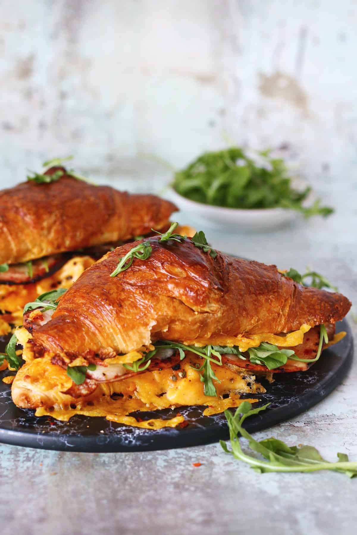 Croissant egg sandwich on a black marble dish with fresh arugula at the back.