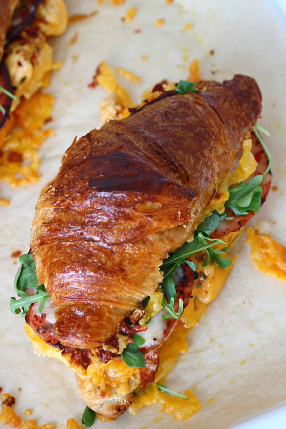 Golden brown toasted top of the croissant sandwich on a parchment paper.