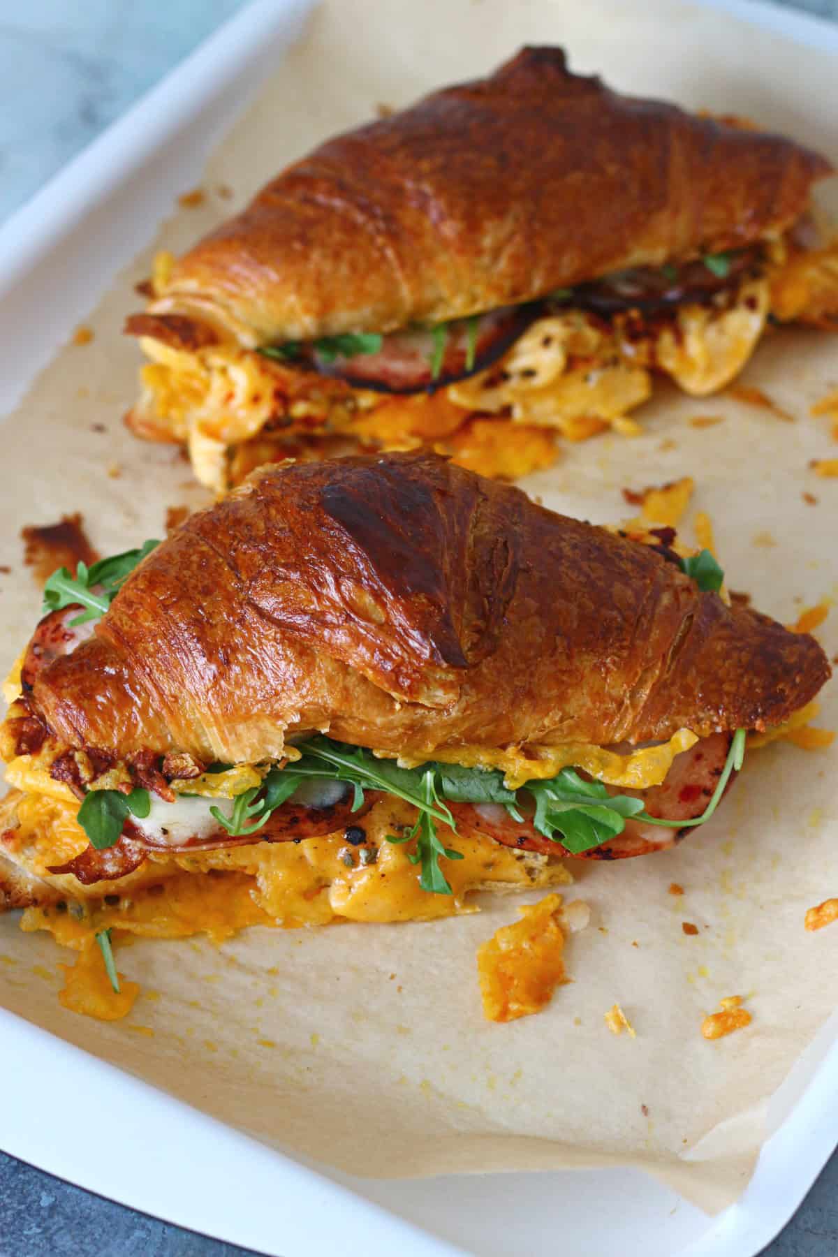 Two toasted croissant egg sandwiches on a baking tray lined with parchment paper.