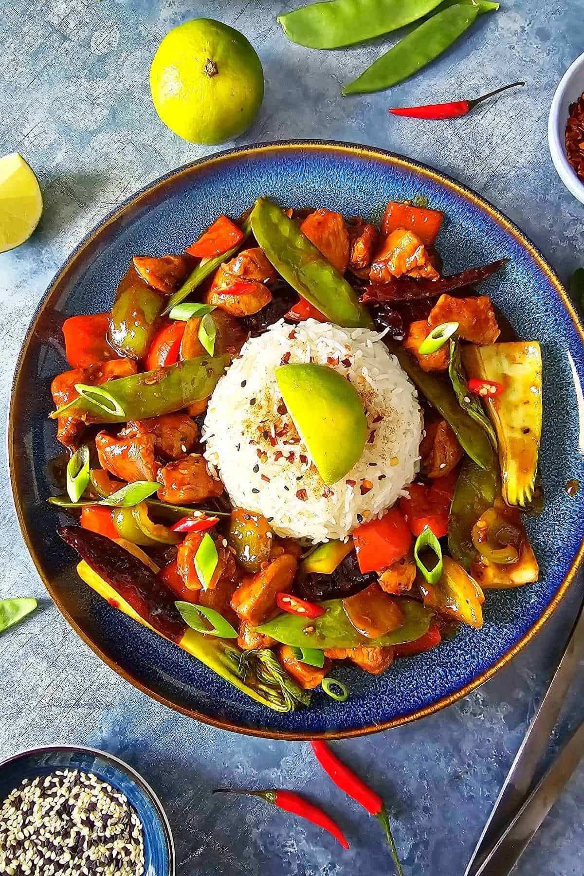 Top view of a plate with a mound of rice surrounded by firecracker chicken stir fry.