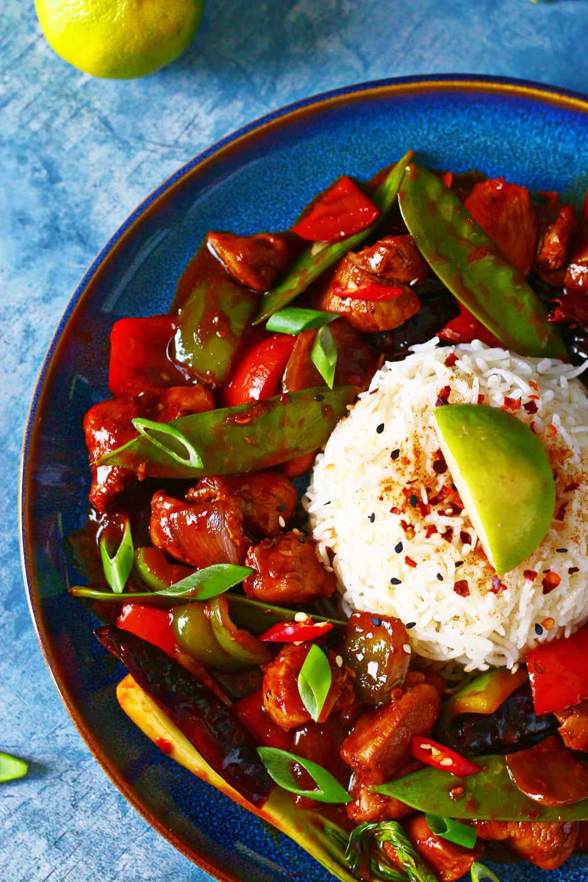 Top shot of half a plate with firecracker chicken and a mound of rice garnished with chili flakes and lime wedge.