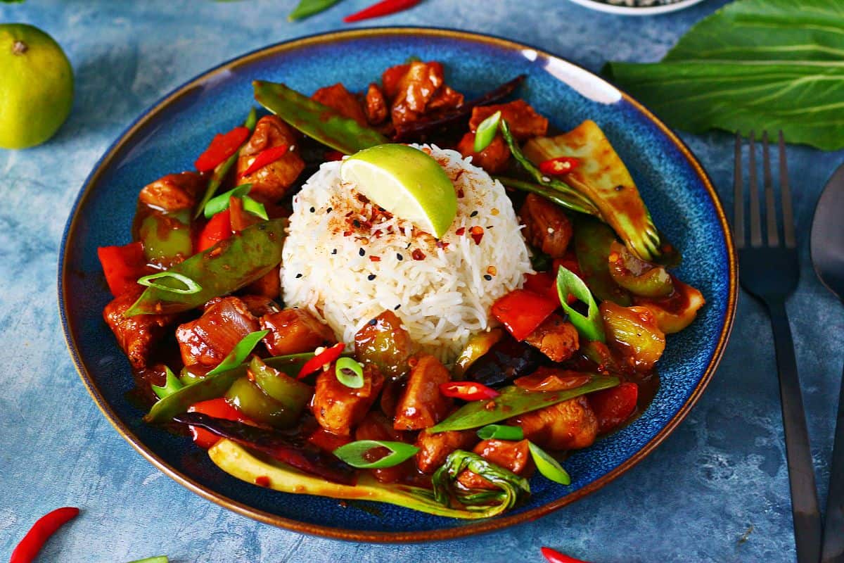 Chicken and vegetable stir fry served with a mound of rice topped with lemon wedge.