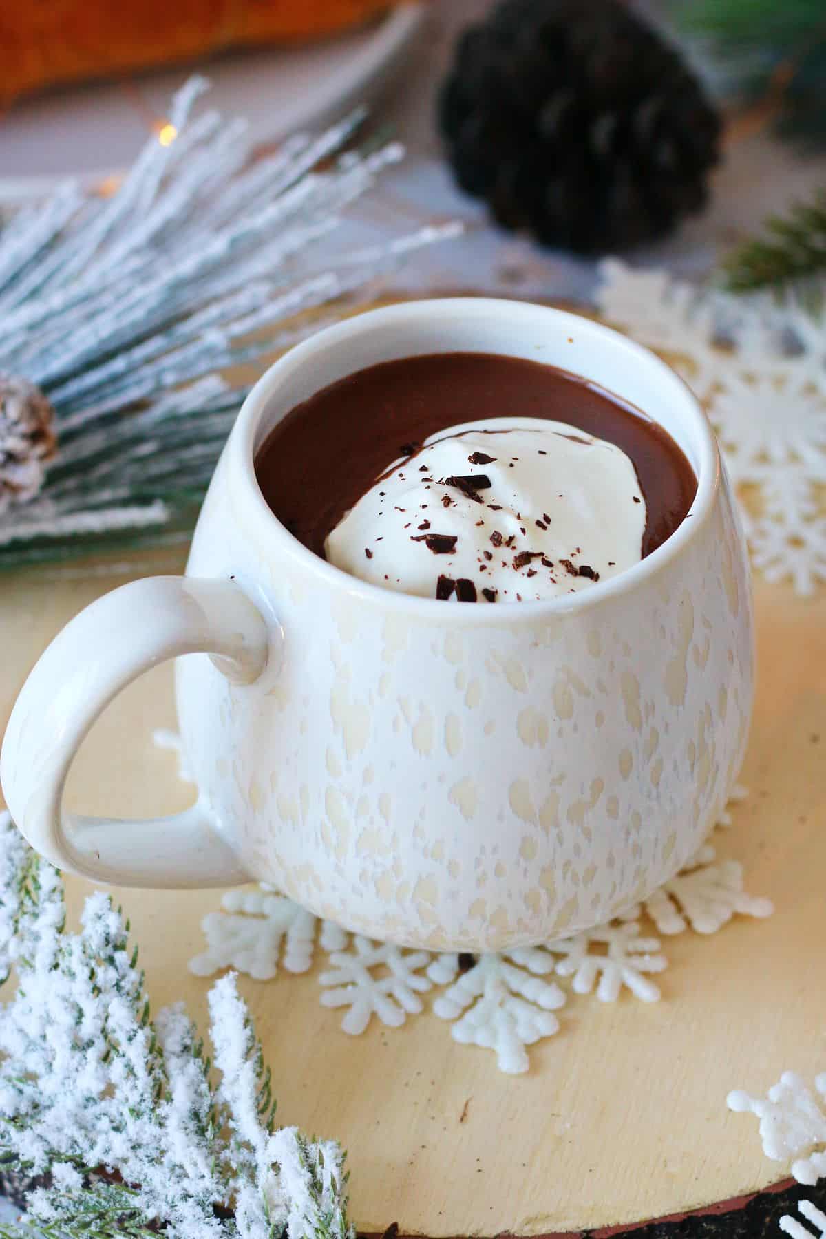 French Hot Chocolate in a white mug topped with whipped cream and chocolate shavings with Winter decor around it.