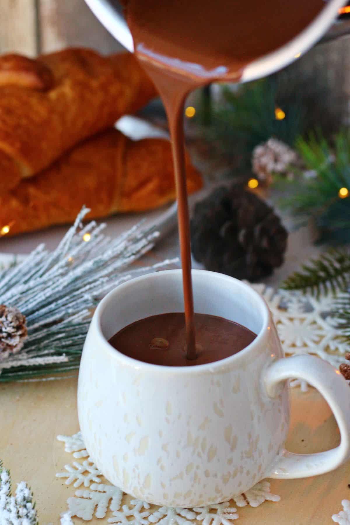 Pouring hot chocolate from a pan into a white mug.