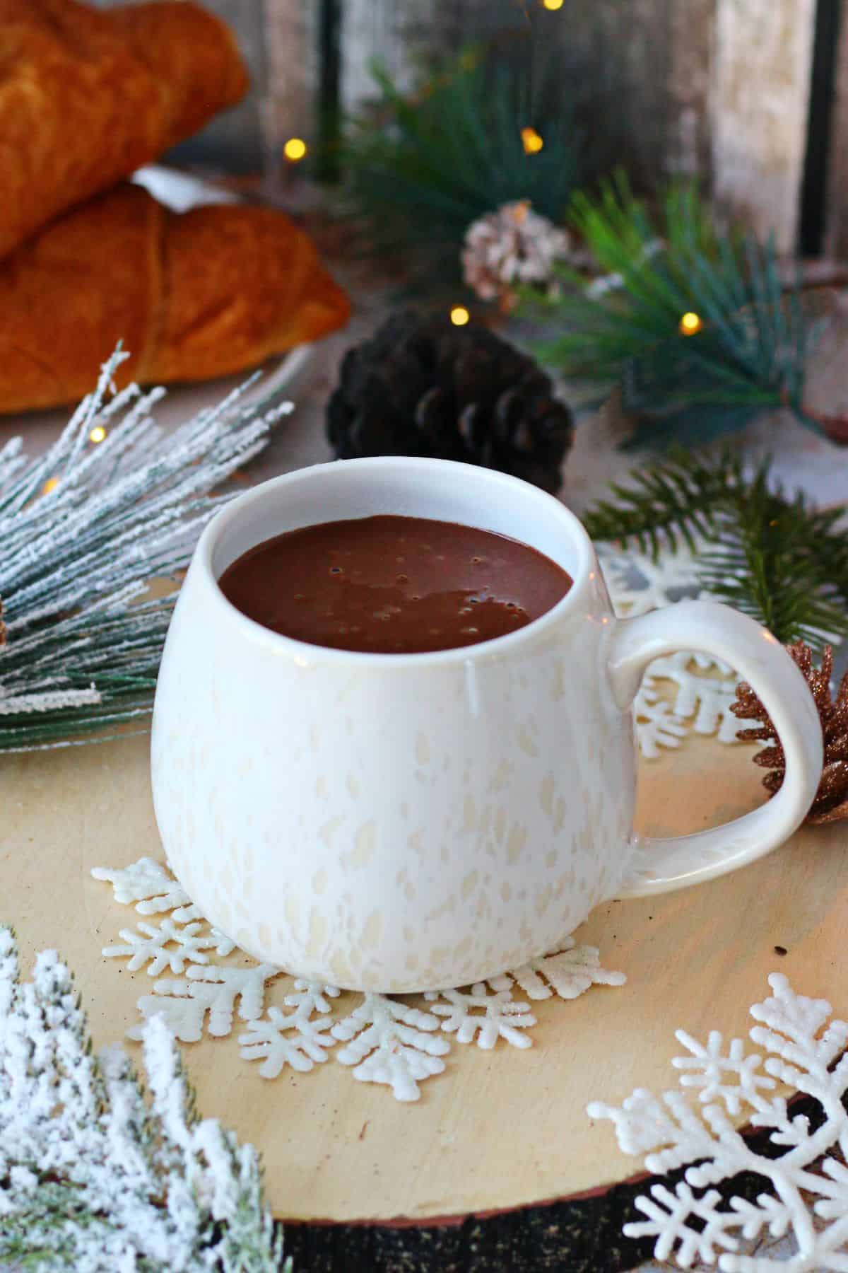 Thick hot chocolate in a white mug with winter decor behind it.