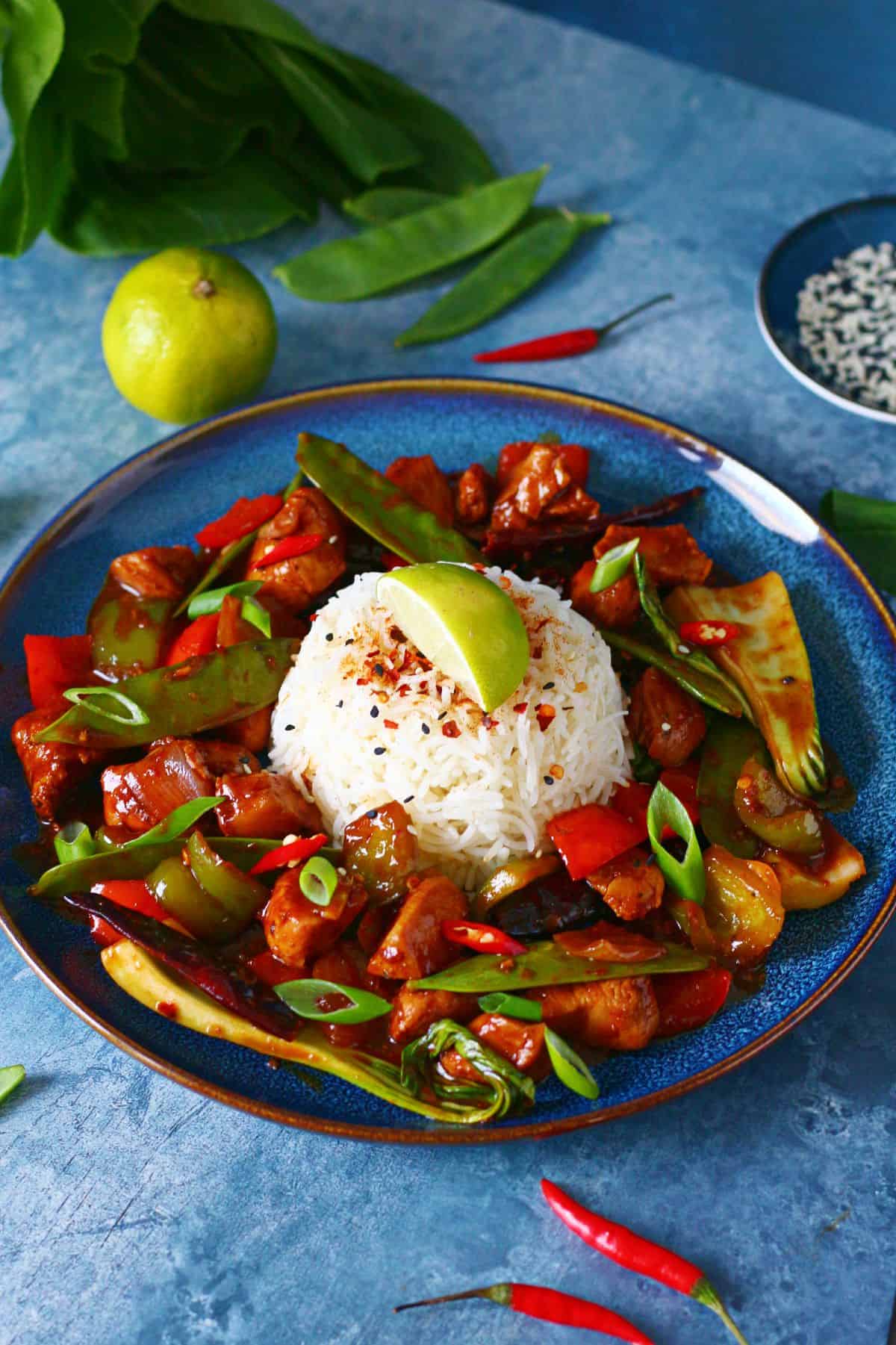 Firecracker chicken on a blue plate with a mound of rice in the middle garnished with a lemon wedge.