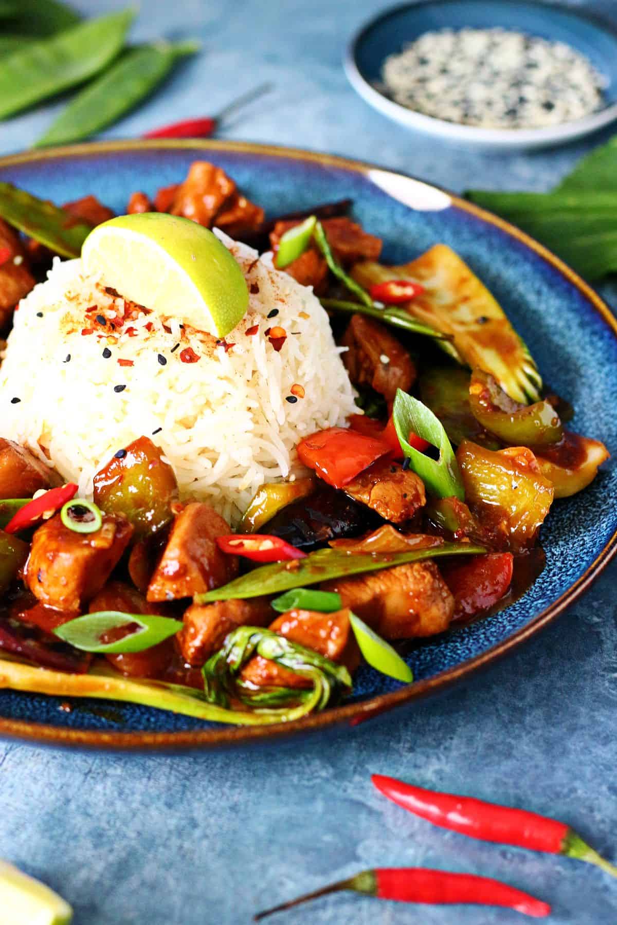 Firecracker Chicken with veggies served with a pile of rice topped with crushed red pepper and lime wedge.