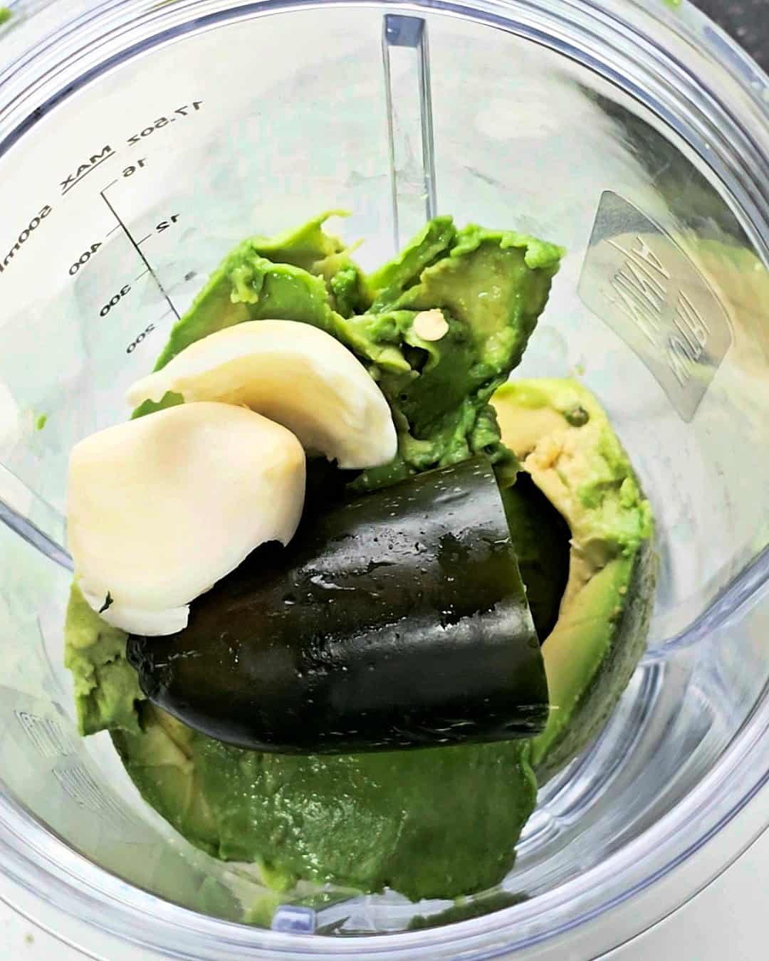 Avocado, jalapeno, garlic cloves in a blender jug.