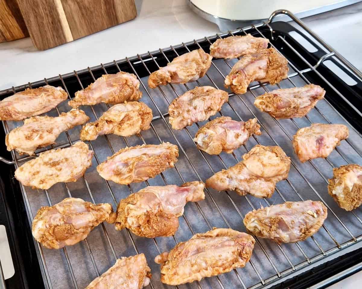 Uncooked chicken wings on a wire rack with a sheet pan at the bottom.