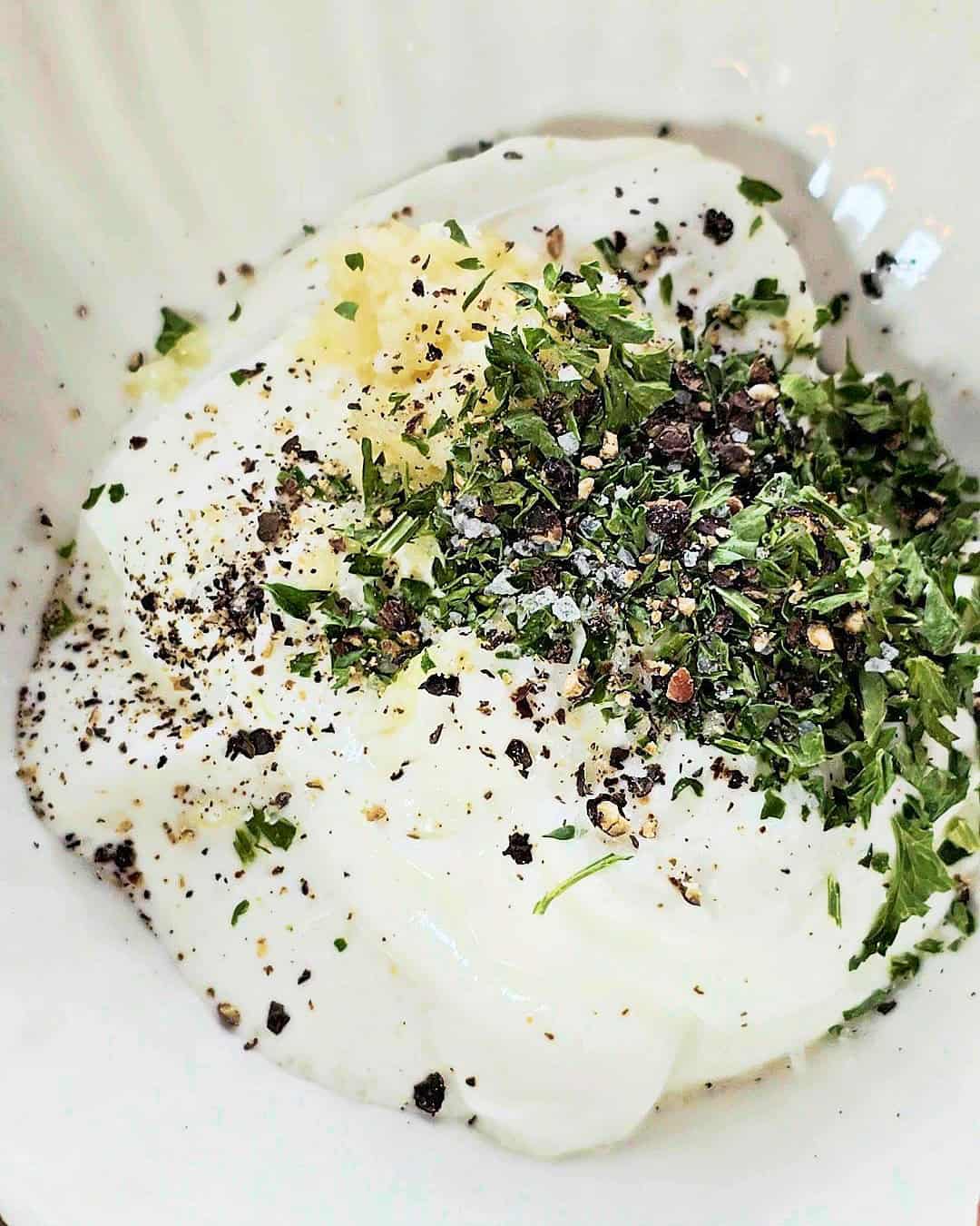 Yogurt with dried parsley, crushed garlic, salt and pepper in a small bowl.