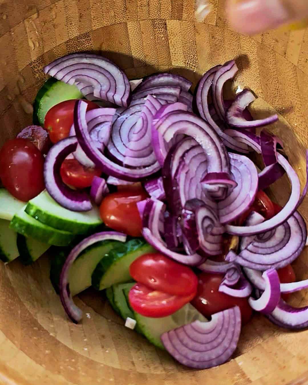 Sliced onions, cherry tomatoes and cucumbers in a brown salad bowl.