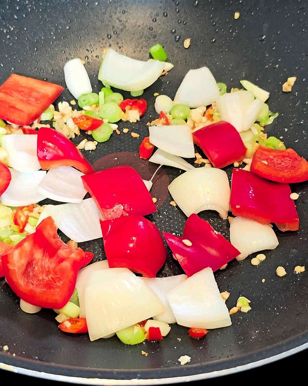 Sauteing cubed red peppers, onions and aromatics in a black wok.