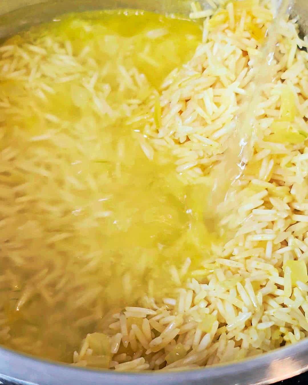 Pouring water into a pot with yellow uncooked rice.