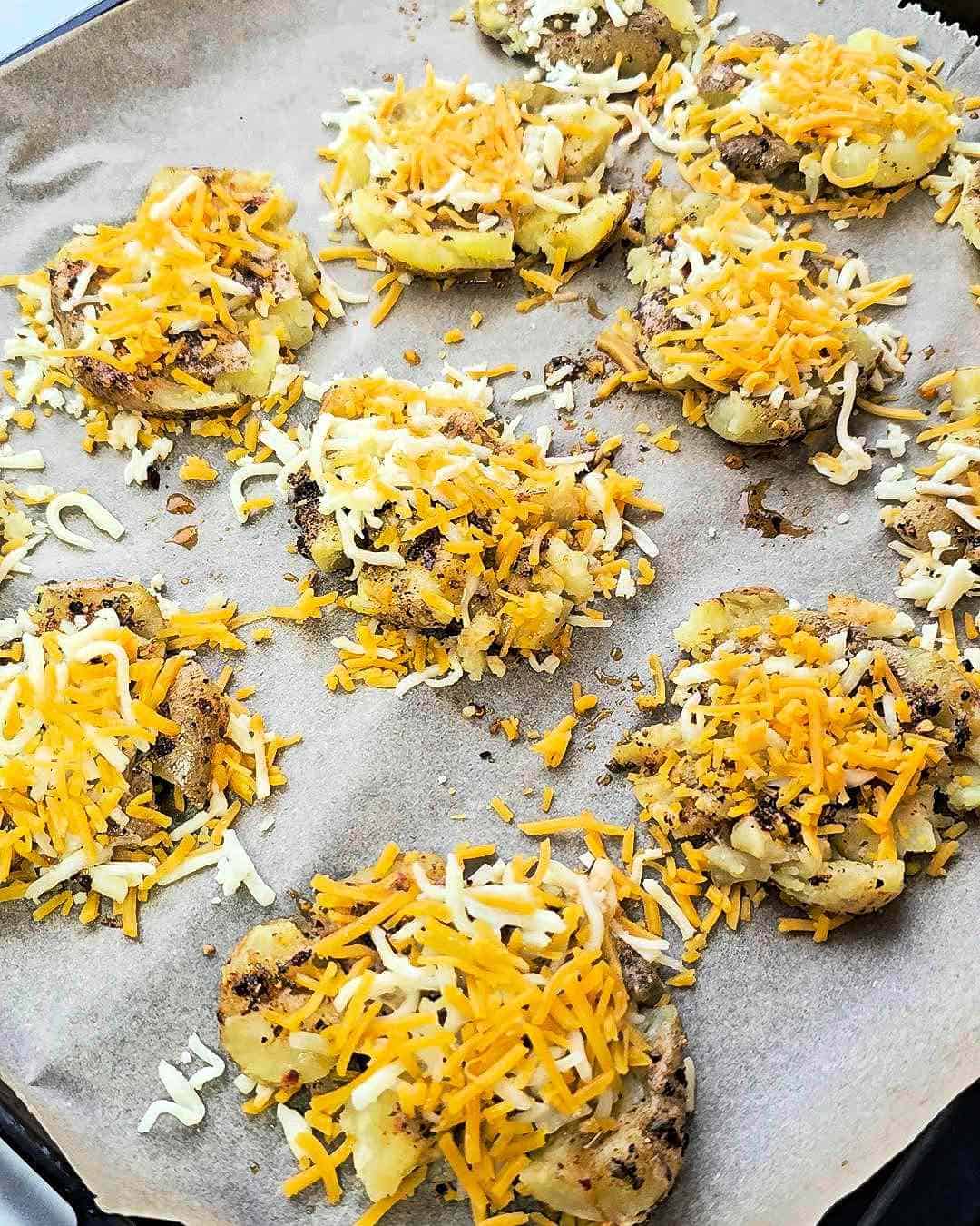 A baking tray with smashed potatoes covered with cheese.