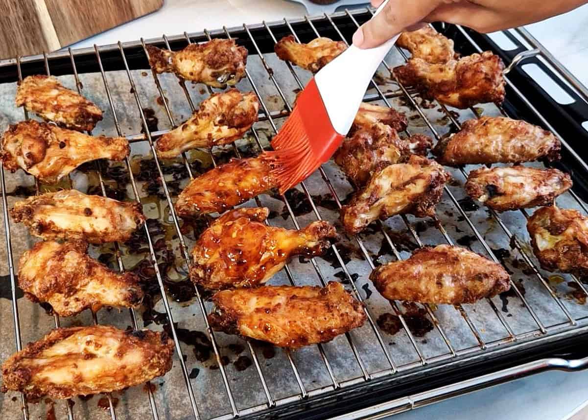 Basting chicken wings with a brush on a wire rack.