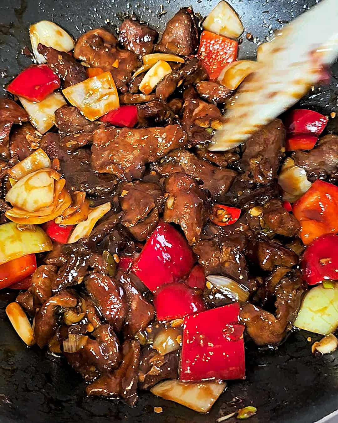 Mixing crispy beef with cubed onions and peppers.