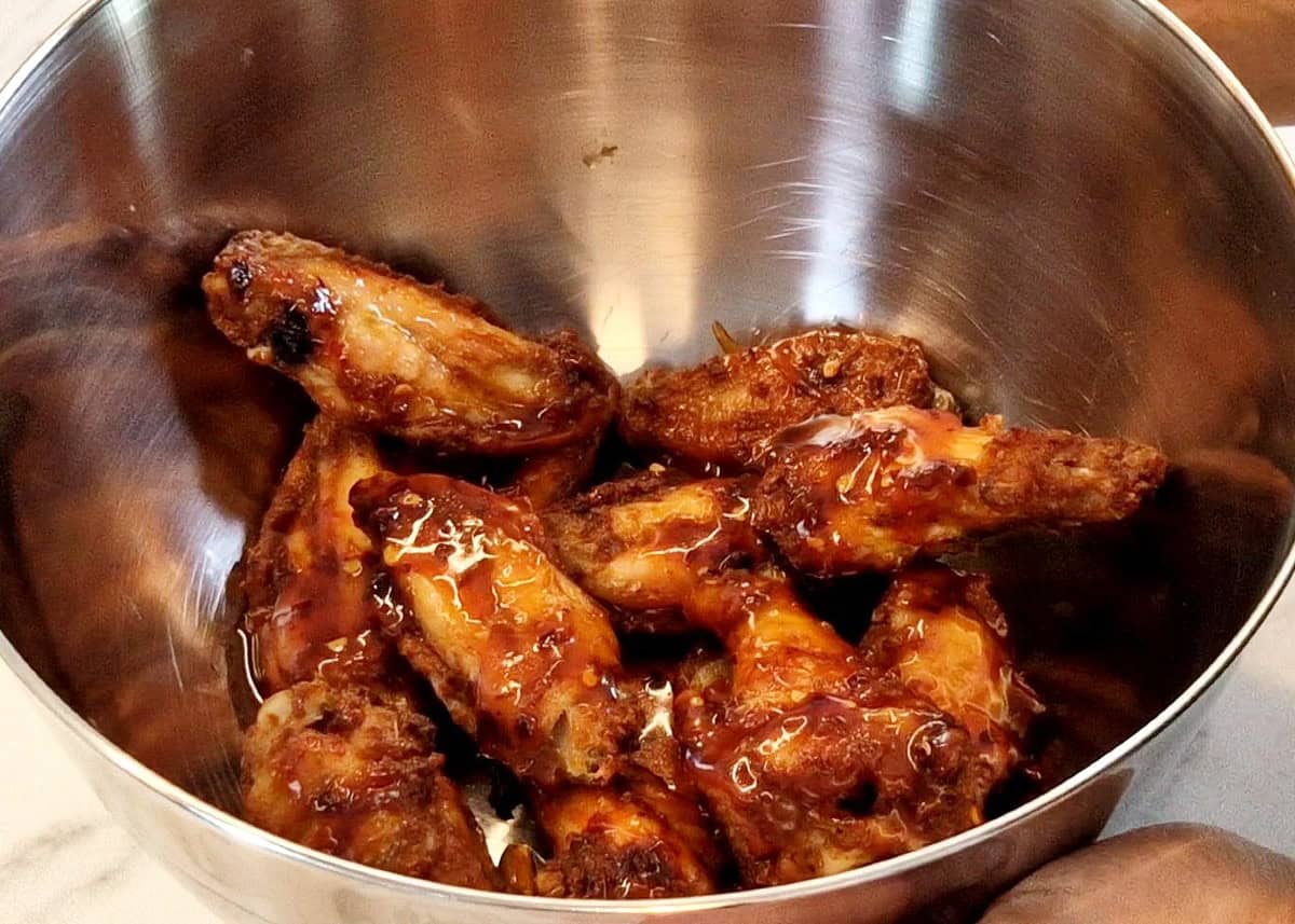 Chicken wings in a steel bowl slathered with sauce.