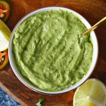 Avocado crema in a white bowl with spoon and a lime wedge on the side.