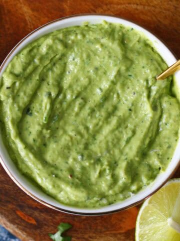 Avocado crema in a white bowl with spoon and a lime wedge on the side.