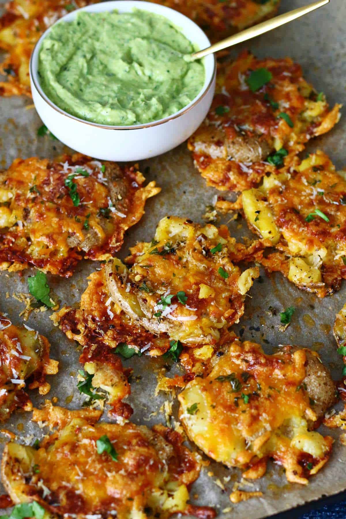 Smashed potatoes on a parchment paper with a bowl of avocado crema on the side.