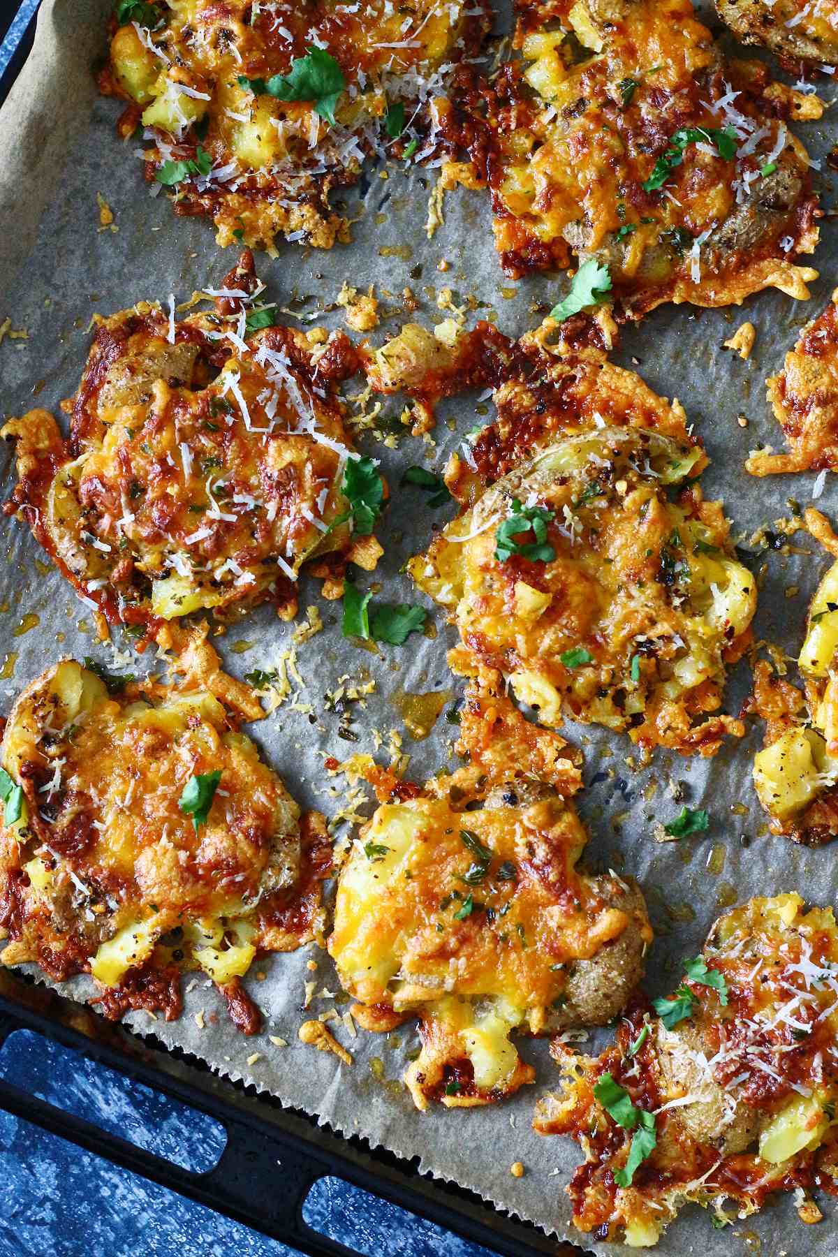 Cheesy smashed potatoes on a parchment paper, garnished with chopped cilantro.