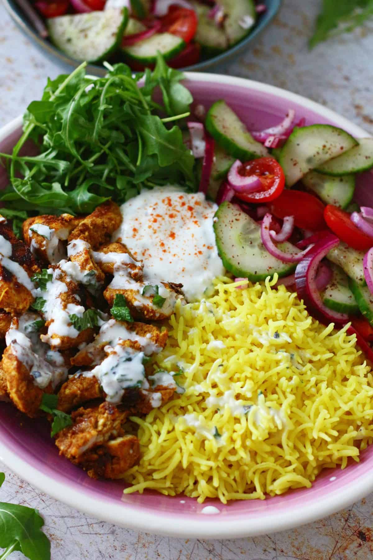 White sauce drizzle on a plate of chicken shawarma with rice and salad.