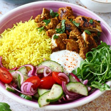 Shawarma chicken, yellow rice, arugula, white sauce and salad in a pink plate.