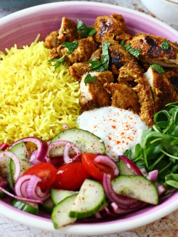 Shawarma chicken, yellow rice, arugula, white sauce and salad in a pink plate.