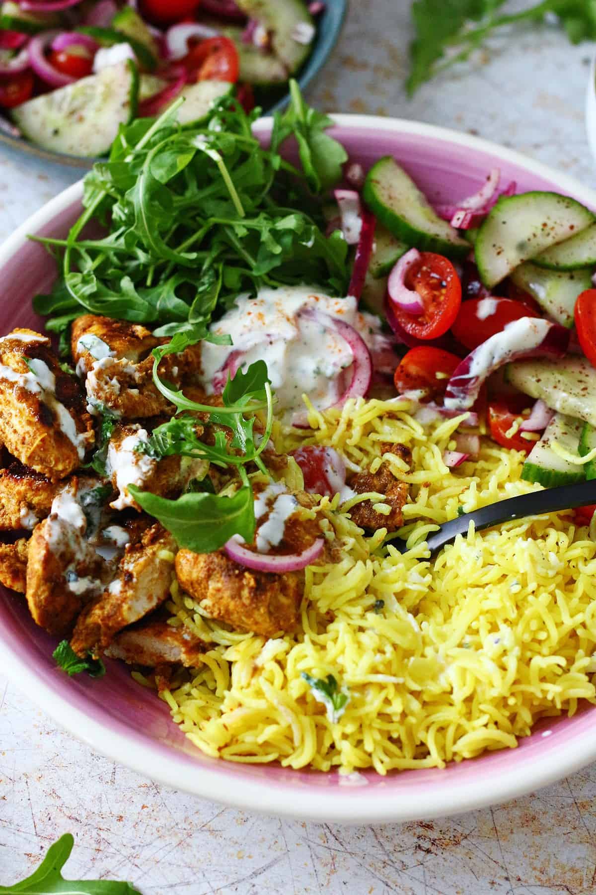 Digging with a fork into a bowl of chicken shawarma with rice and salad.