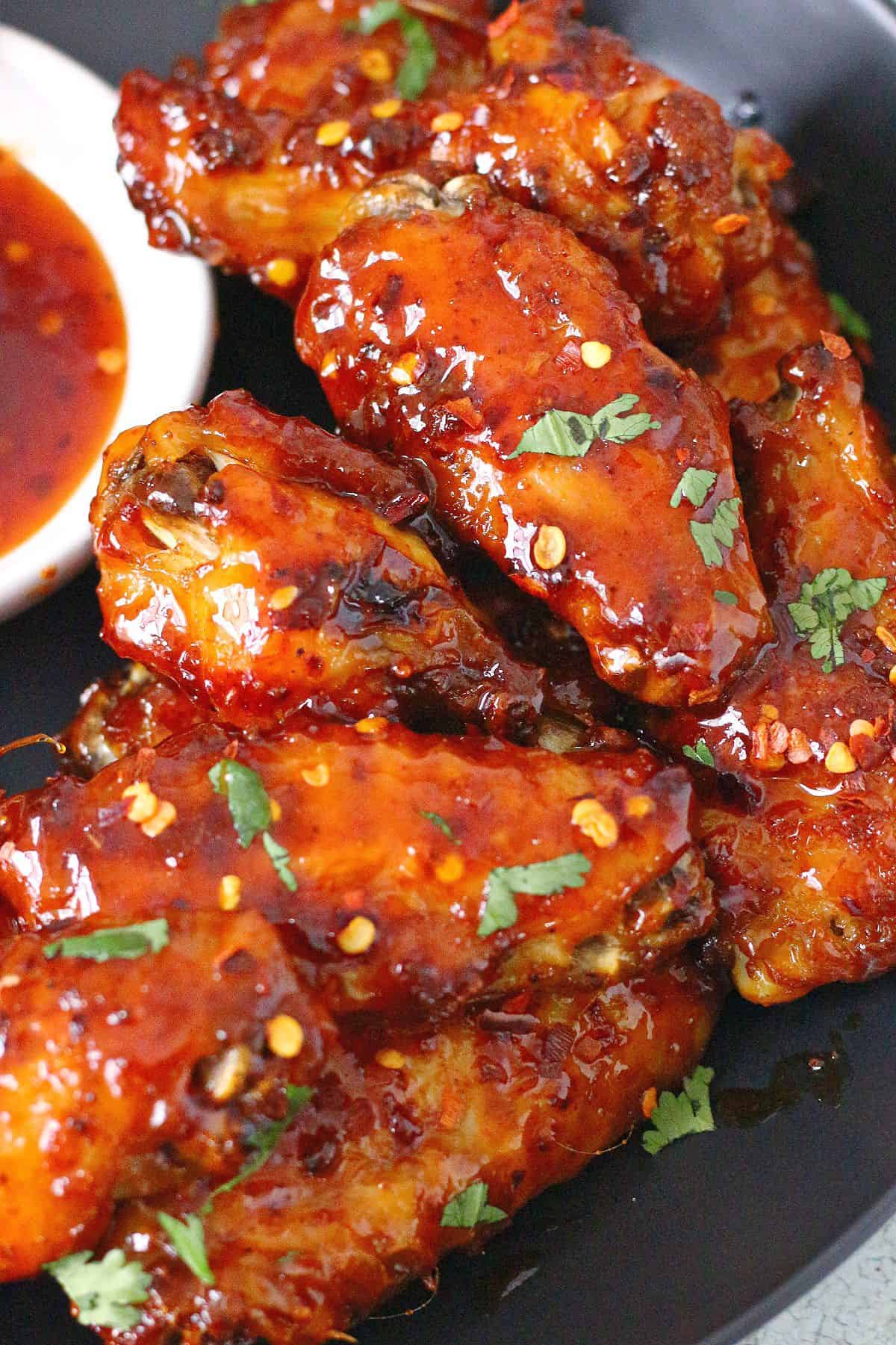 Sticky chicken wings garnished with chopped cilantro on a black plate.