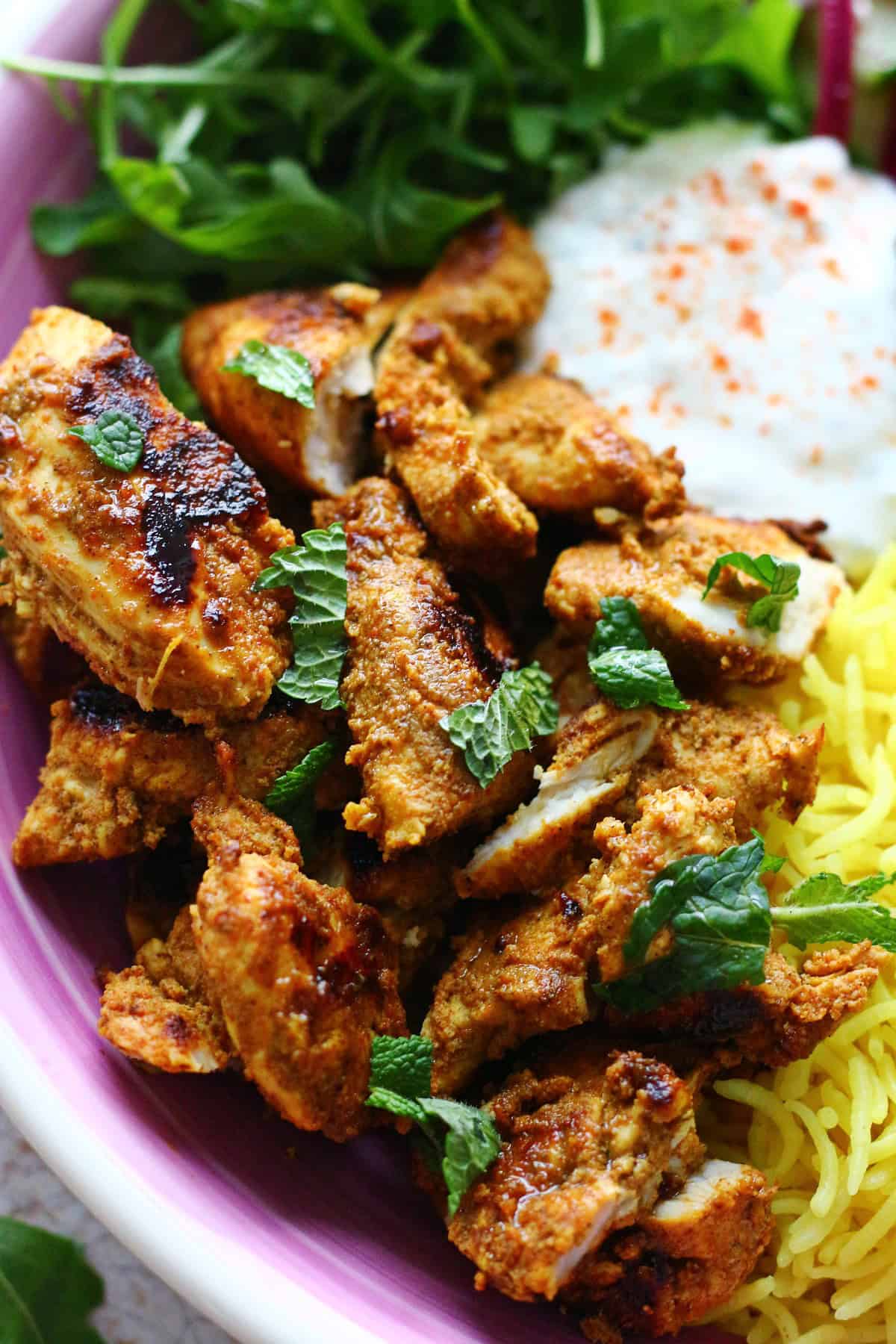 Close up of sliced grilled chicken garnished with chopped mint.